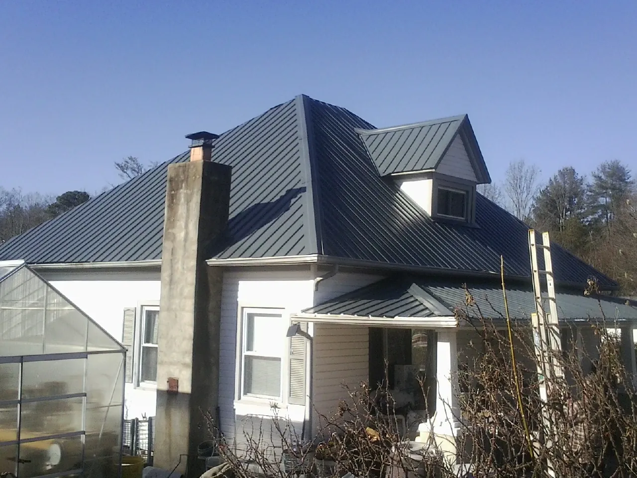 Dark blue standing seam metal roof on a white farmhouse with dormer — Slate & Tile Roof Repair by Roofing Brothers in Blue Jay