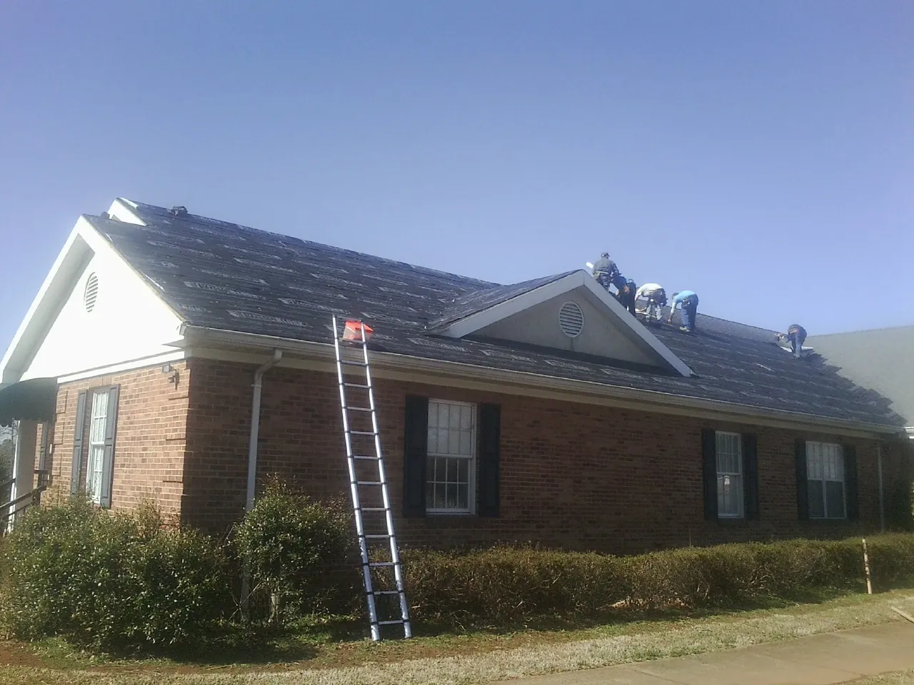 Crew tearing shingles off a brick ranch roof with a ladder set — Metal Roof Repair work by our crew in Blue Jay