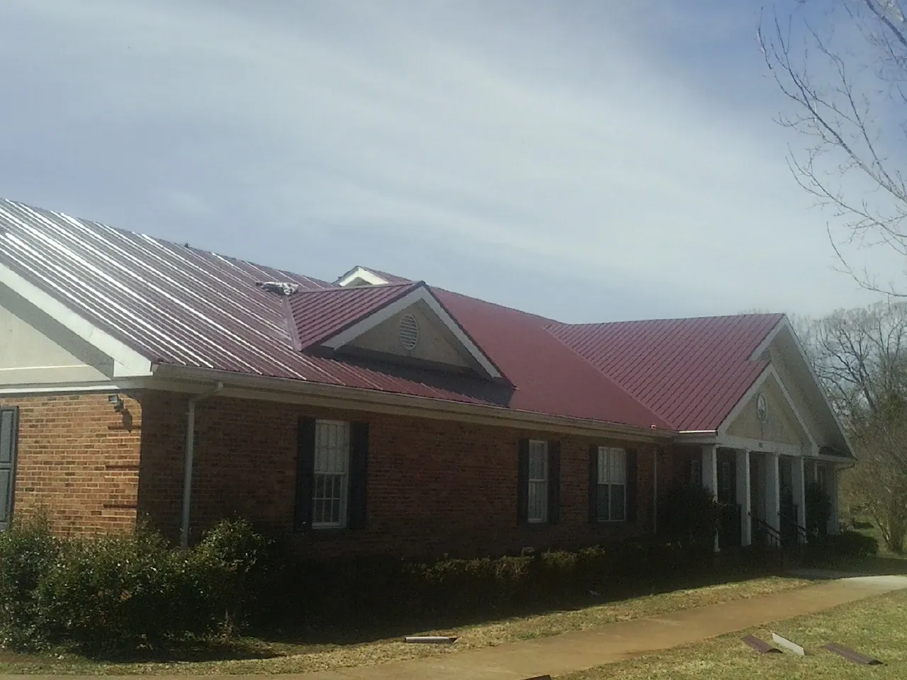 Red metal roof with gabled entries on a long brick building, from a Hail Damage Roof Repair job in Blue Jay