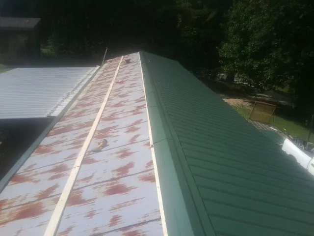 Old rusted panels beside newly installed green metal roofing — Wind Damage Roof Repair by Roofing Brothers in Blue Jay