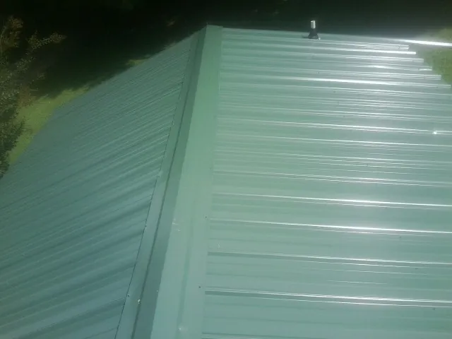 New green metal panels meeting at the ridge of a roof — Flat Roof Repair work by our crew in Blue Jay