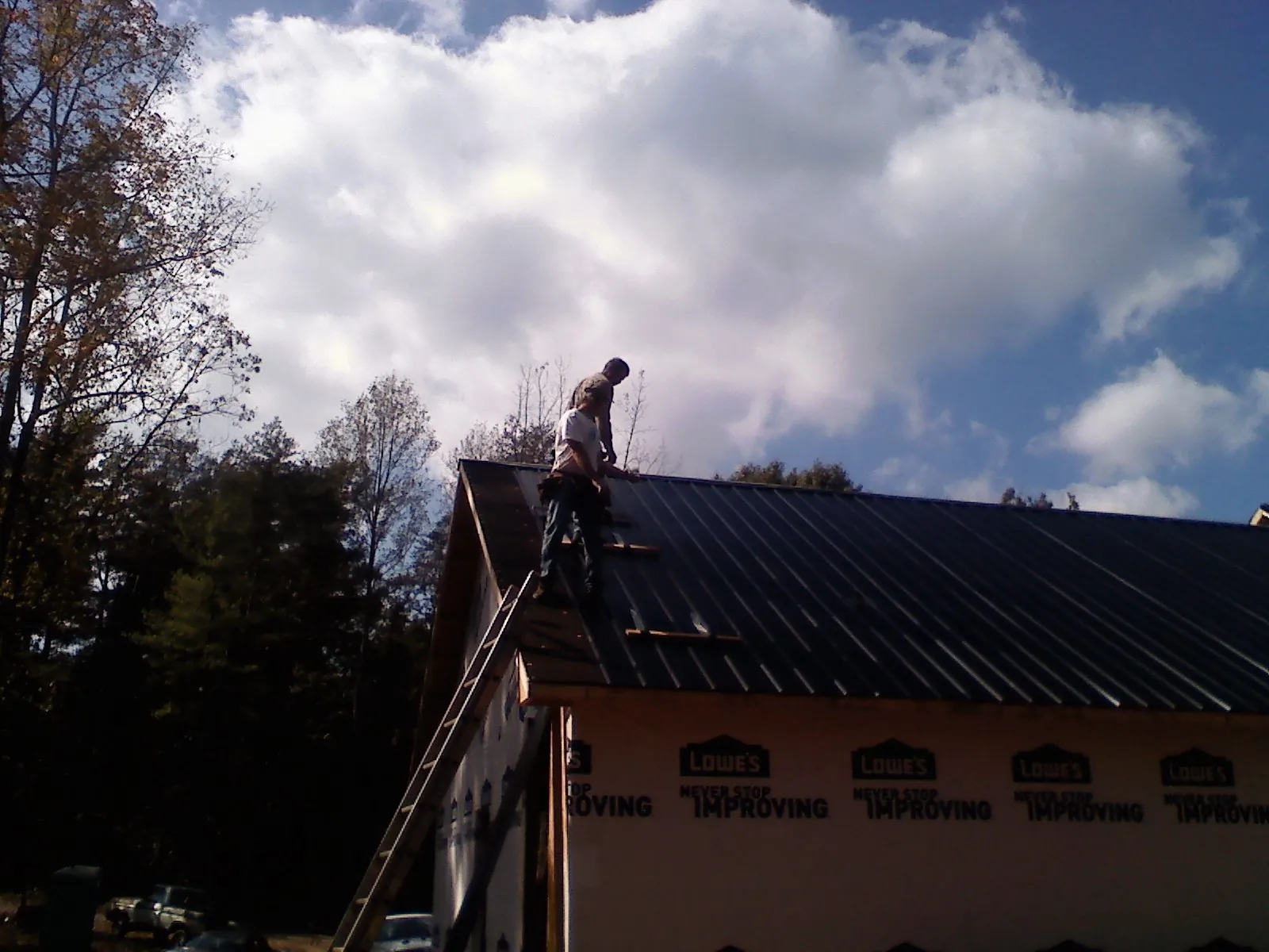 Roofer fastening dark metal panels high against a cloudy sky, from a Roof Inspection job in Blue Jay